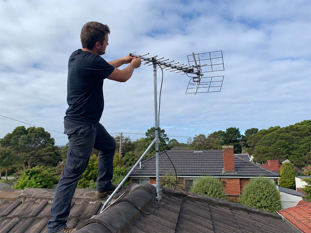 Technician adjusting a rooftop TV antenna on a suburban Melbourne home for digital TV reception.